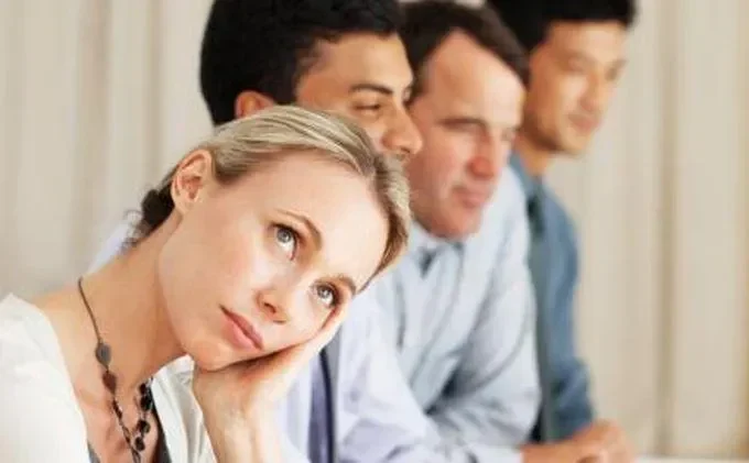 Wanita bosan dalam rapat, dikelilingi pria berjas.