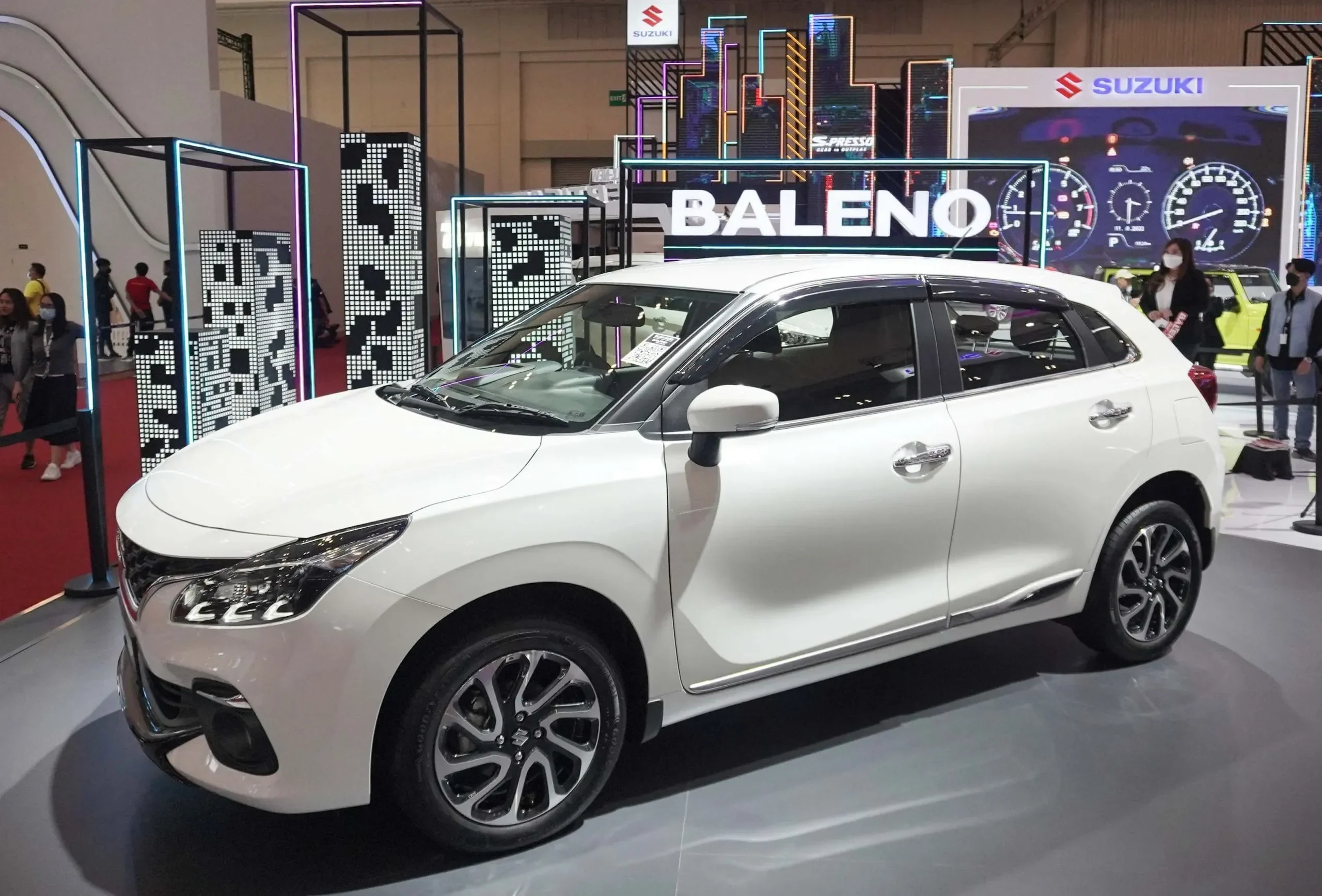 Suzuki Baleno Hatchback putih terparkir di pameran otomotif dengan latar belakang logo Suzuki.