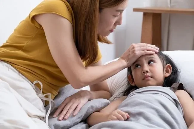 Ibu memeriksa suhu tubuh anak yang sakit di ranjang.