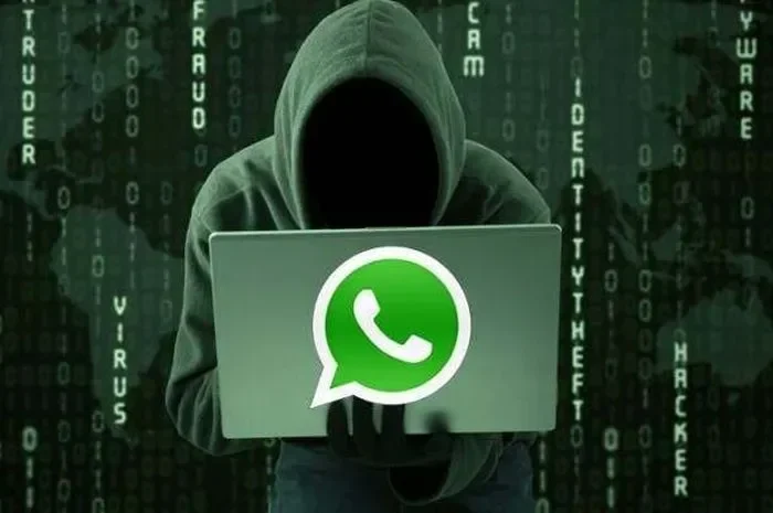 Seorang peretas misterius memegang laptop dengan logo WhatsApp, mengancam keamanan data online.