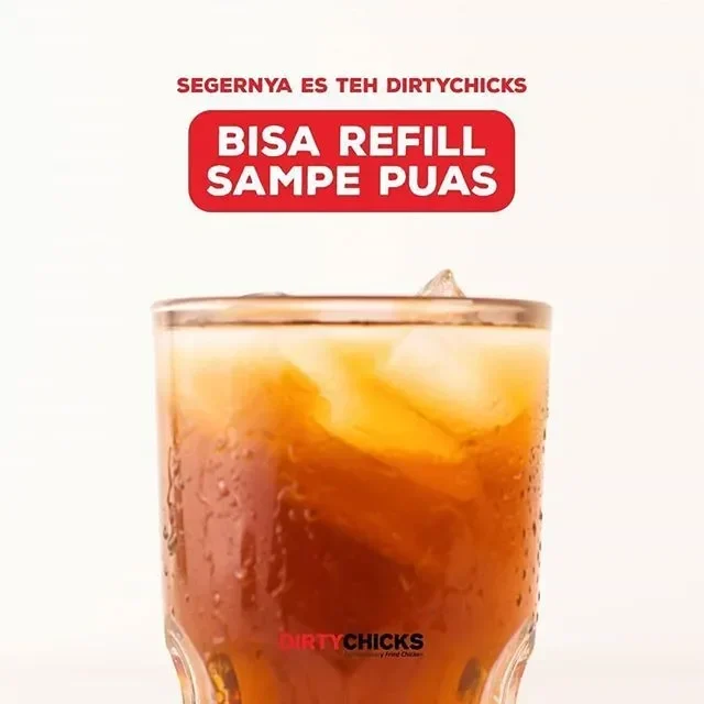 Segelas es teh manis di samping ayam goreng siap disantap.