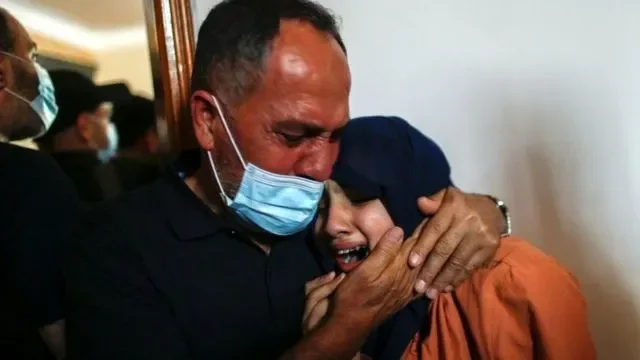 Dua orang, seorang pria bermasker dan wanita berhijab, berpelukan dalam kesedihan di Gaza.