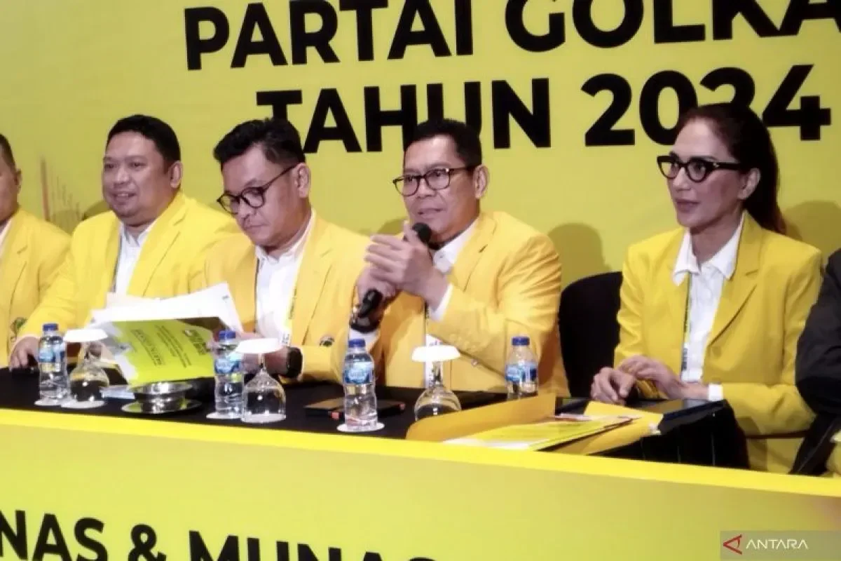 Panelis diskusi politik mengenakan jas kuning di depan spanduk Partai Golkar, salah satunya memegang mikrofon.
