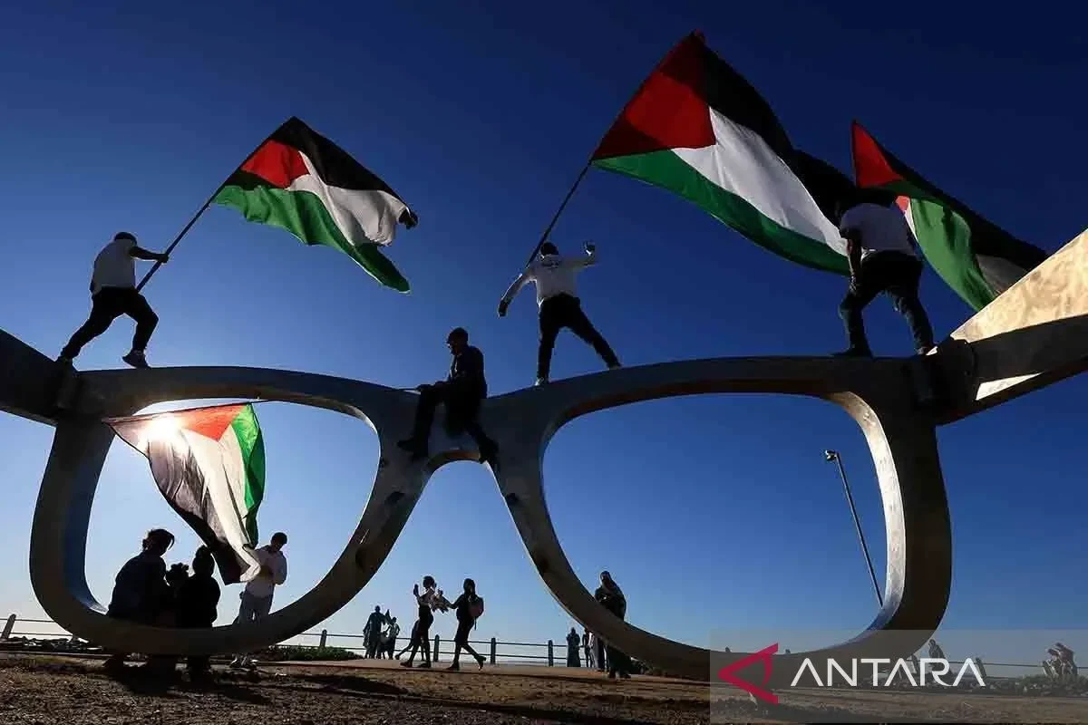 Pengunjuk rasa Palestina kibarkan bendera di atas struktur kacamata raksasa.