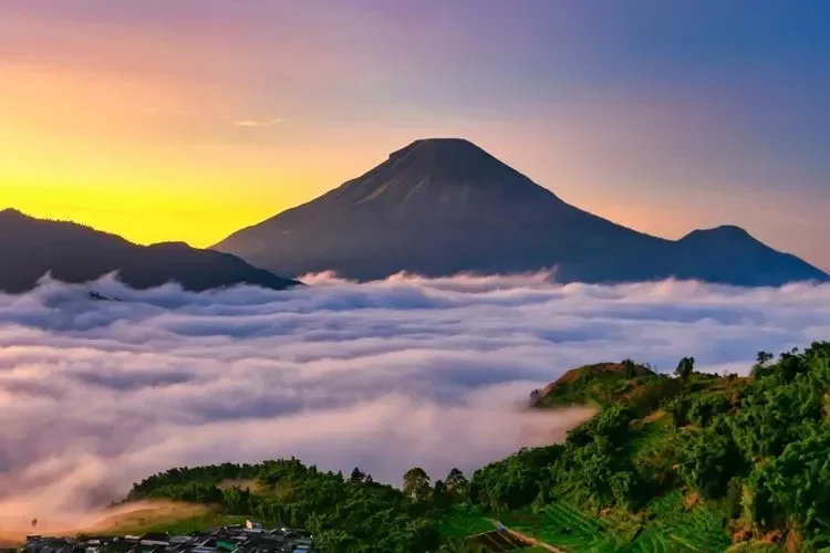 Keindahan Geopark Nasional Dieng dengan gunung menjulang dan lautan awan di bawah langit cerah.