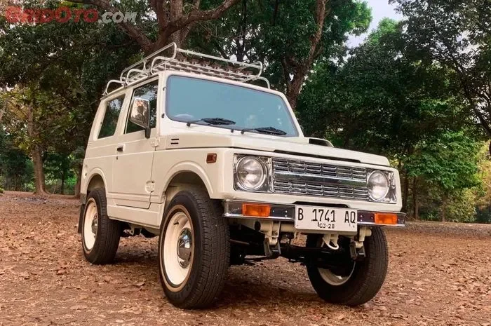 Suzuki Jimny putih klasik terparkir di luar ruangan dengan latar pohon rindang.
