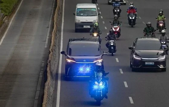 Mobil dan motor dengan lampu strobo biru di jalan raya perkotaan.