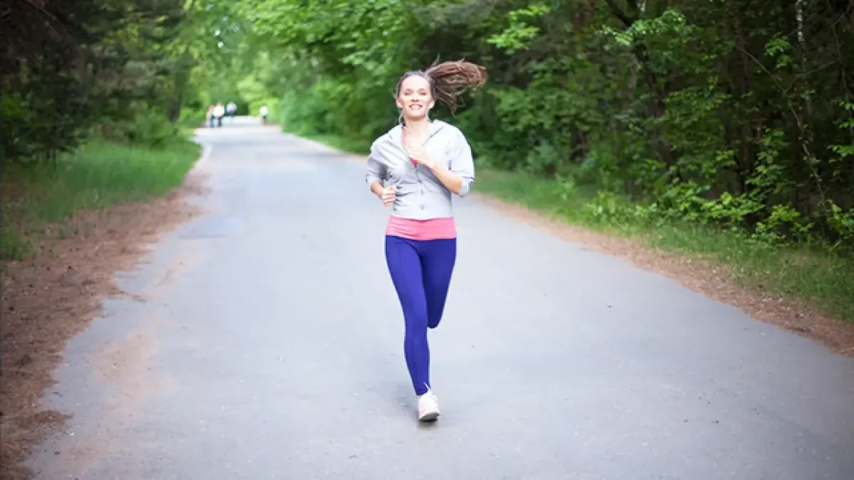 Wanita berlari di jalan setapak di tengah pepohonan hijau, menikmati alam.