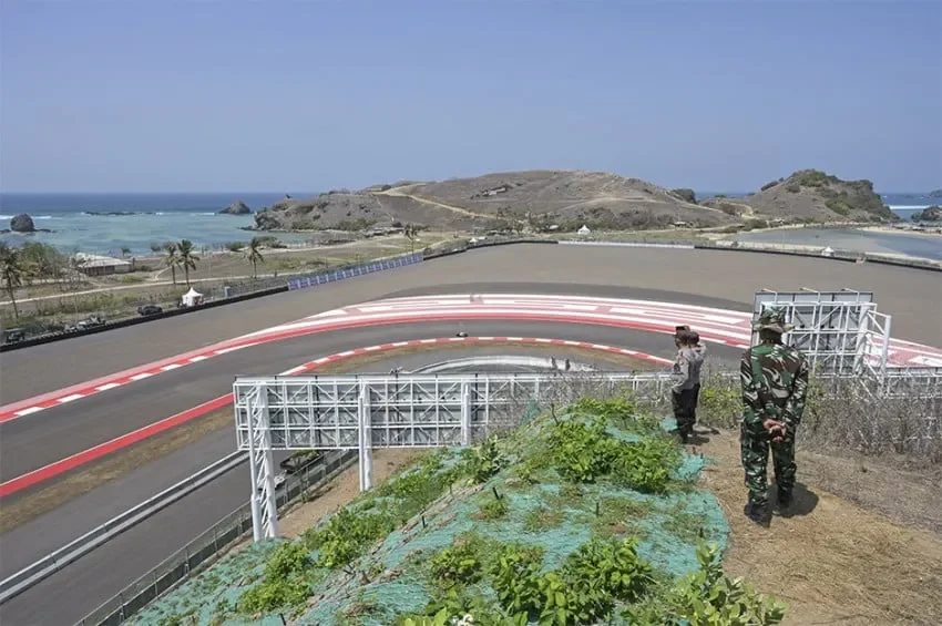 Sirkuit Mandalika dengan latar laut biru, bukit, dan dua orang di gardu pandang.