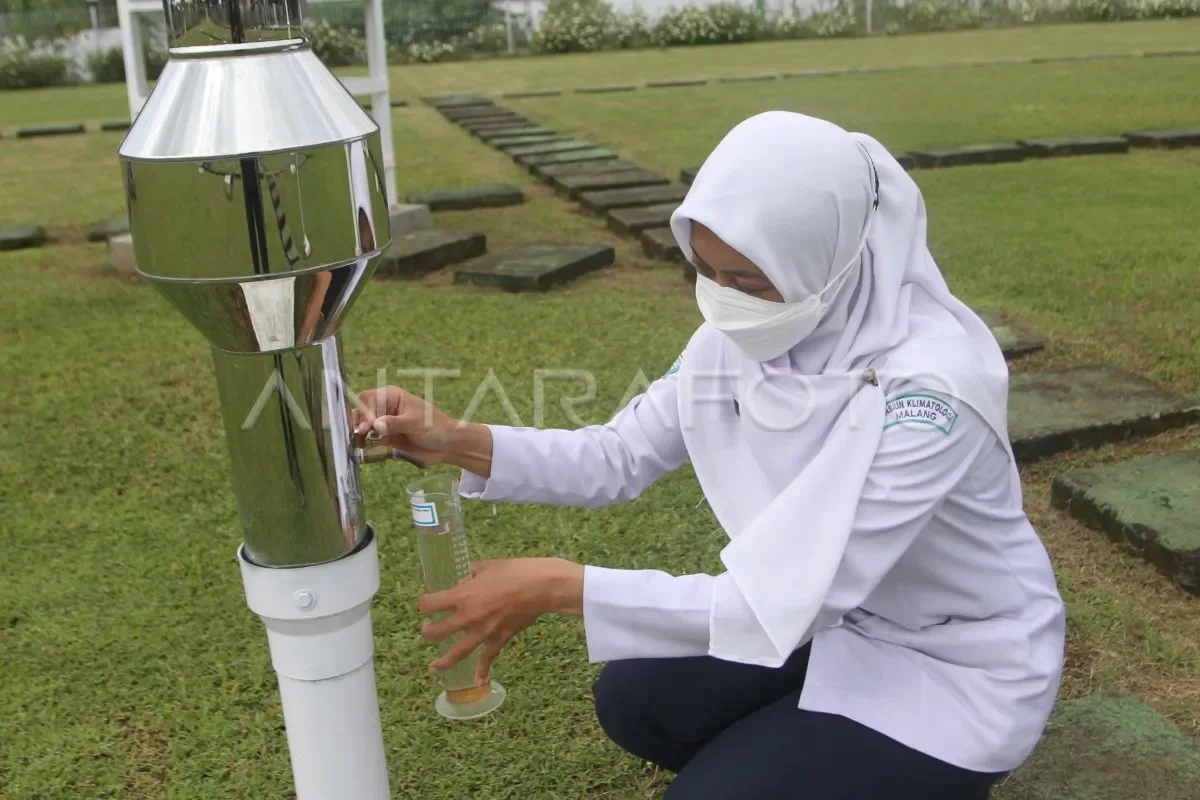 Petugas BMKG mengukur volume air hujan dari ombrometer di stasiun meteorologi.