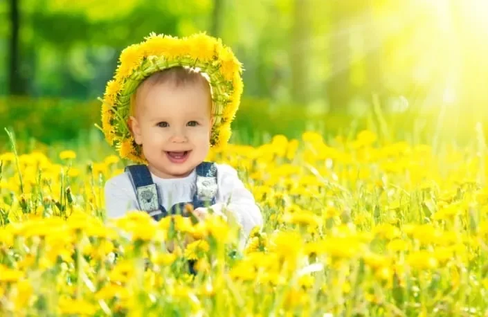 Bayi tersenyum ceria bermahkota bunga kuning di hamparan bunga dandelion.