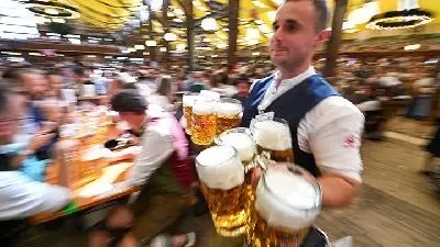 Pelayan membawa gelas bir berbusa di festival Oktoberfest yang ramai.