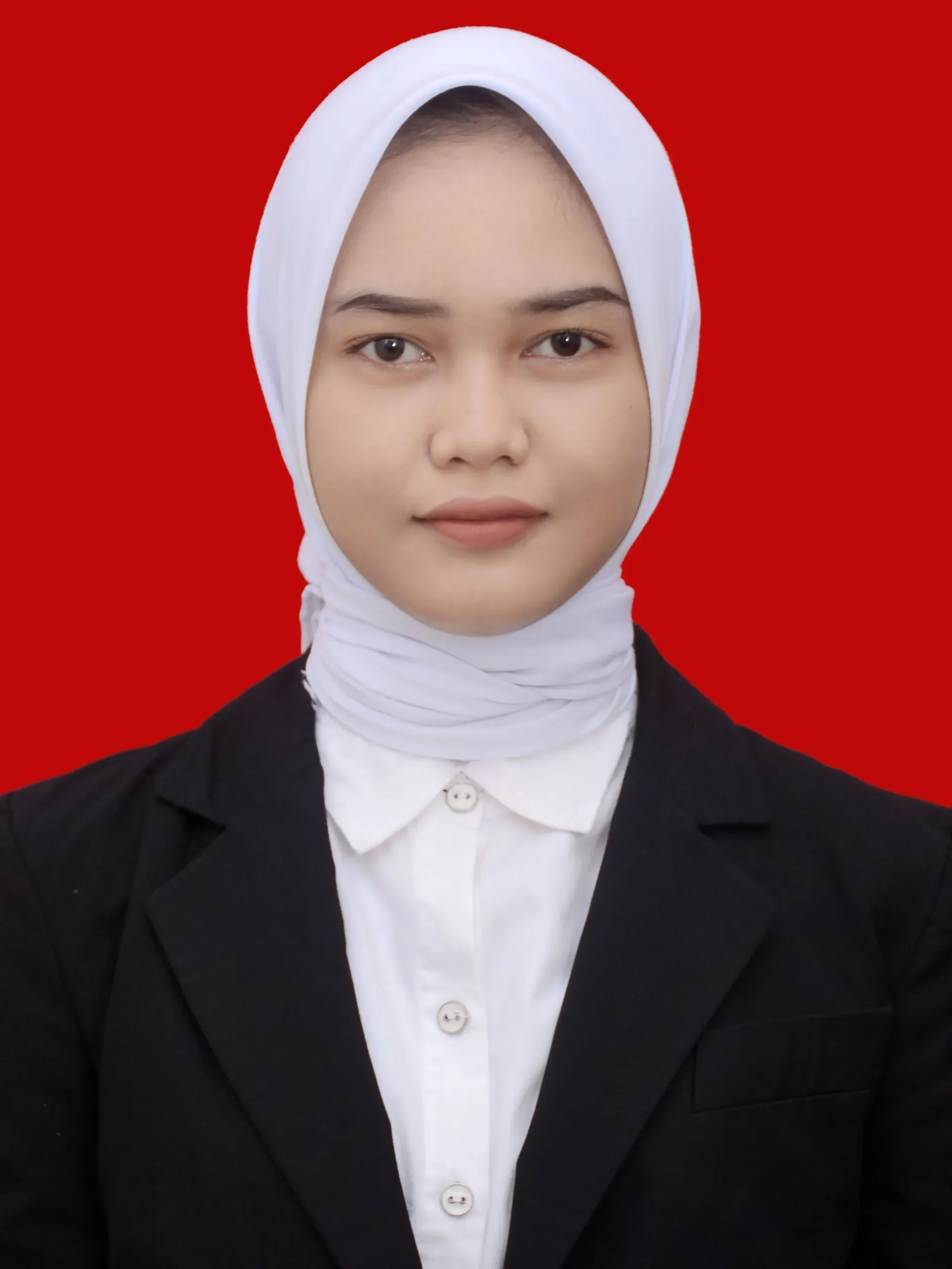 Wanita berhijab mengenakan blazer hitam dan kemeja putih di depan latar merah.