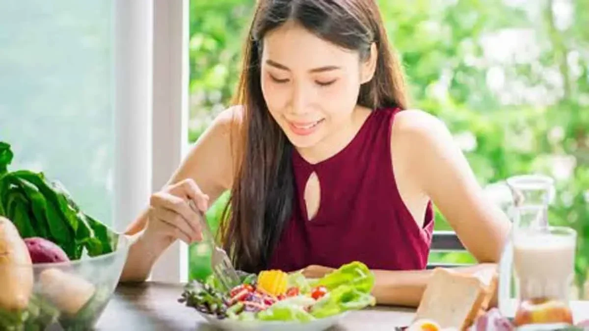 Wanita Asia menikmati salad segar di meja dengan sayuran dan roti.