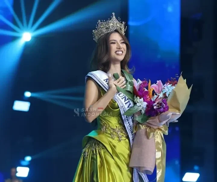 Sanly Liu Miss Universe Indonesia 2025 mengenakan mahkota dan gaun hijau sambil memegang buket bunga.