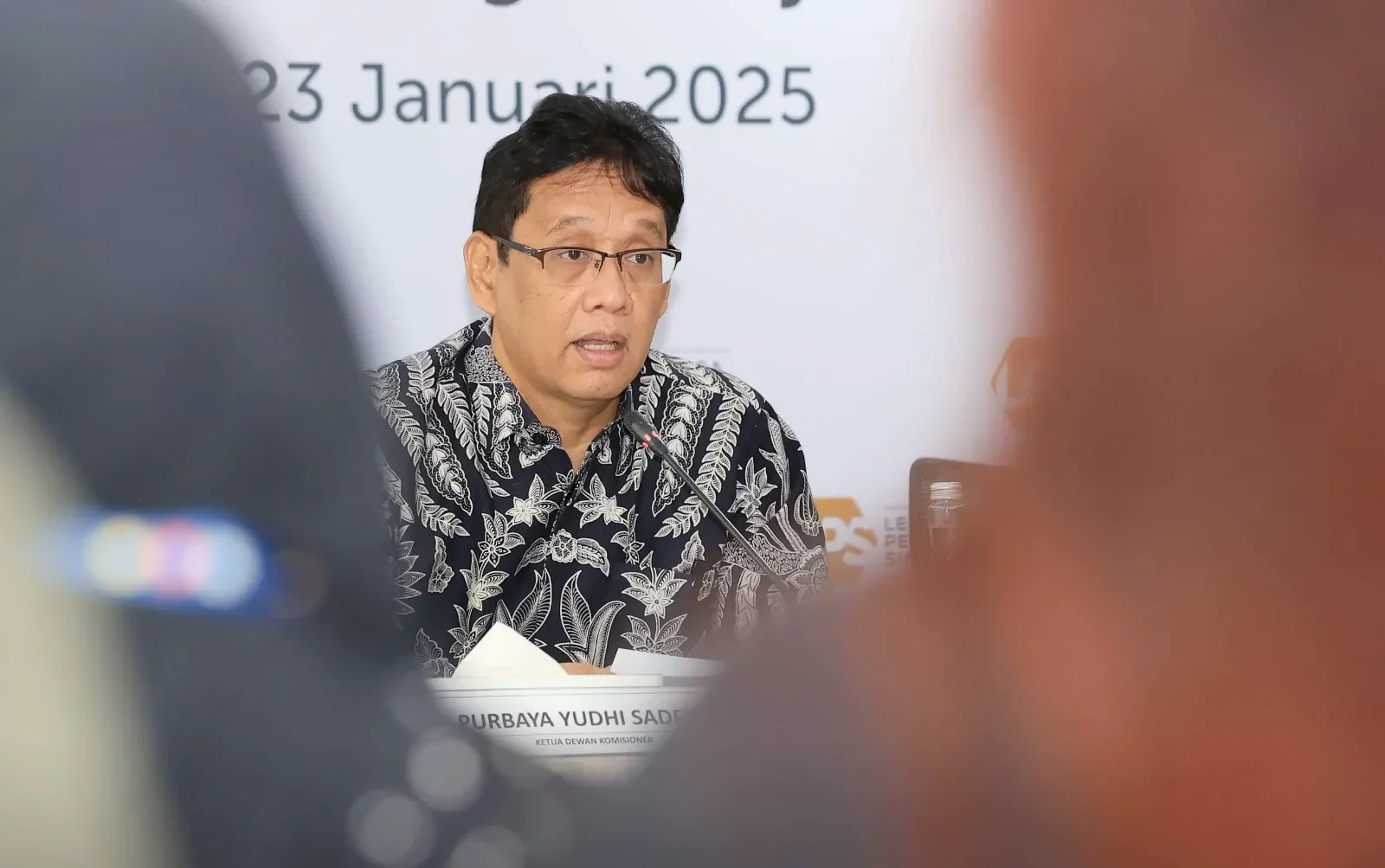 Purbaya Yudhi Sadewa berbicara di hadapan mic, latar belakang putih bertuliskan 23 Januari 2025.