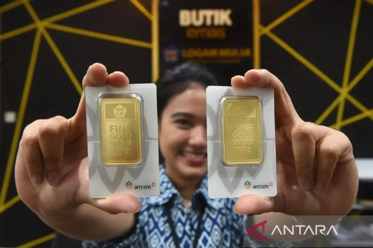 Dua keping emas Antam 100 gram dipegang di depan Butik Emas Logam Mulia.