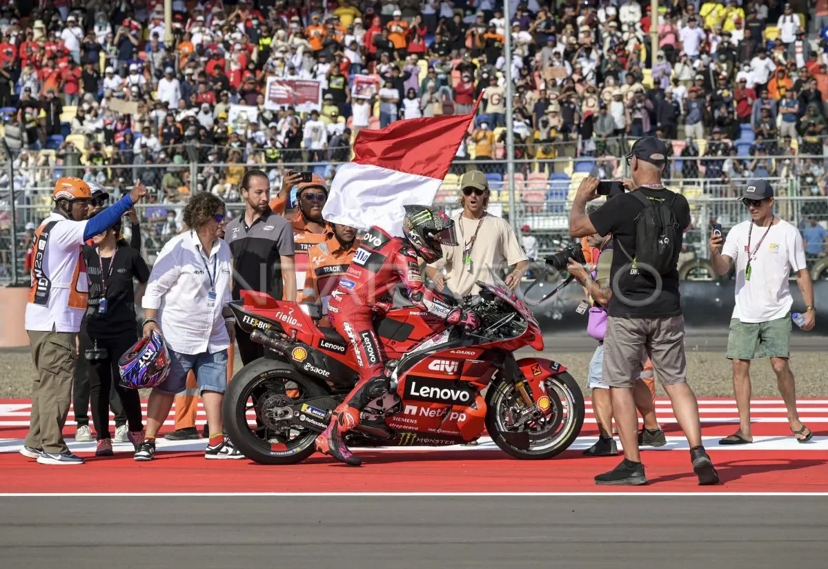 Pembalap Ducati di atas motor, kibaran bendera Indonesia, kerumunan penonton MotoGP.