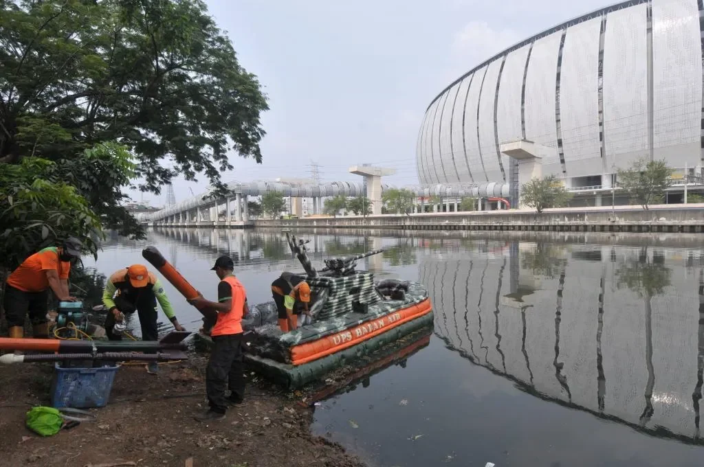 Petugas sedang bersiap membersihkan kali dengan perahu karet di dekat stadion megah.