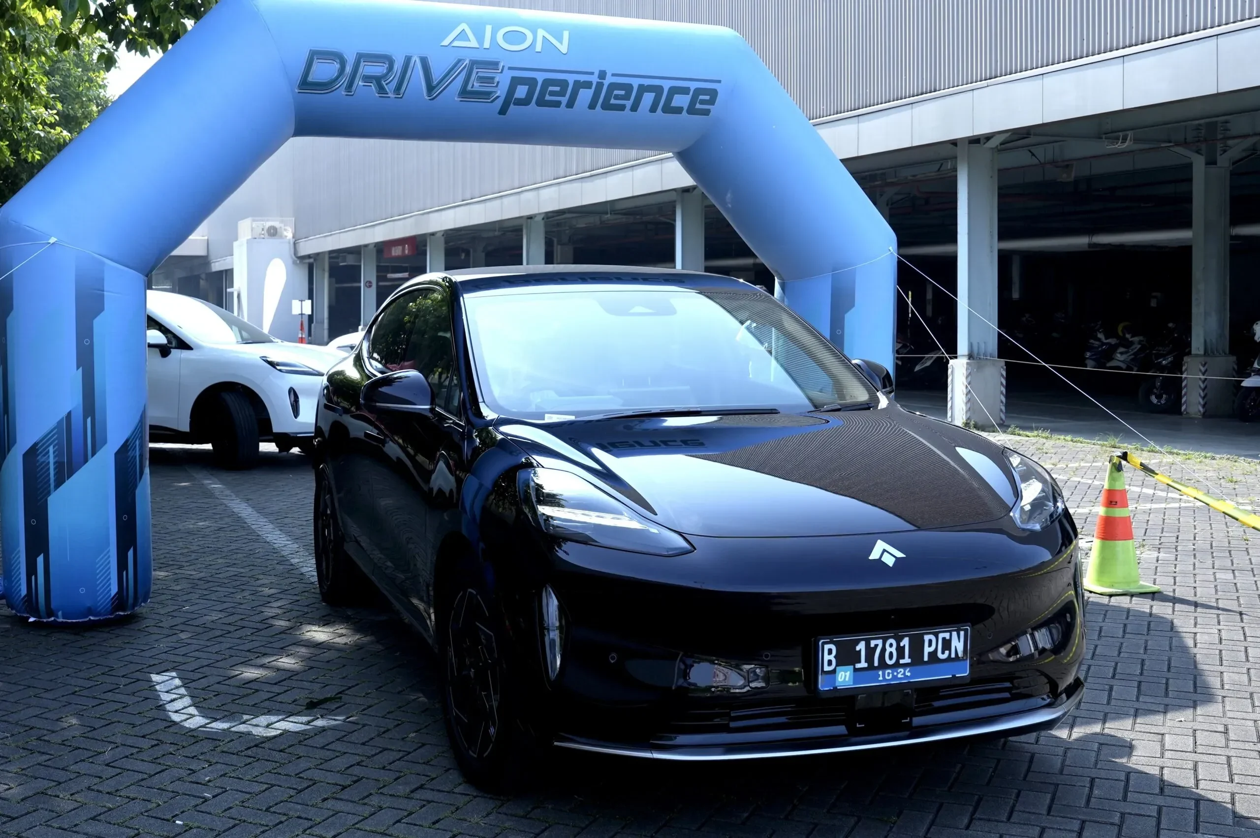Mobil listrik hitam terparkir di bawah gapura biru AION DRIVEexperience.