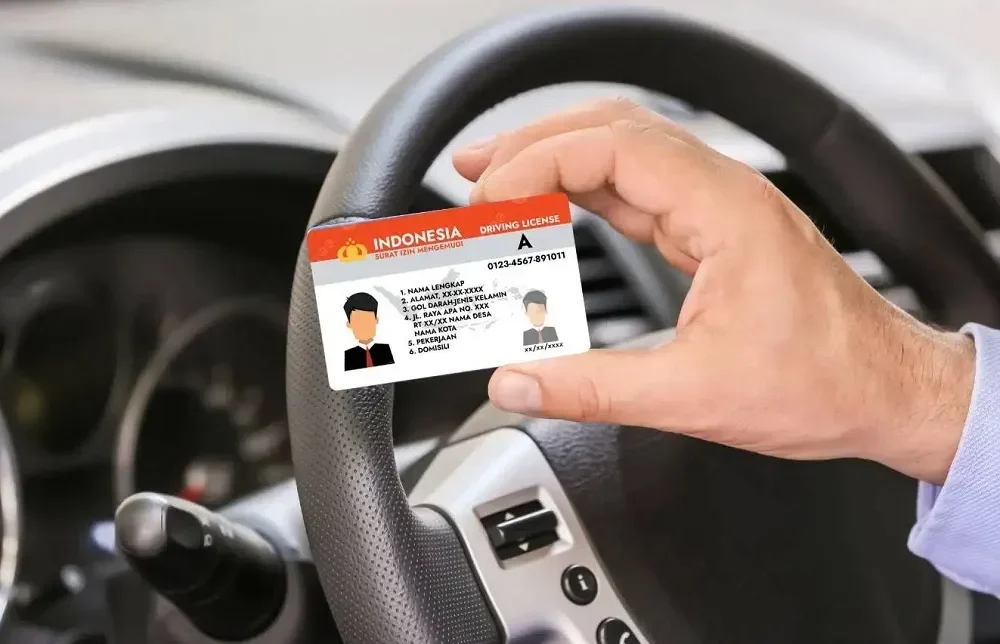 Tangan memegang Surat Izin Mengemudi (SIM) Indonesia dengan latar setir mobil.