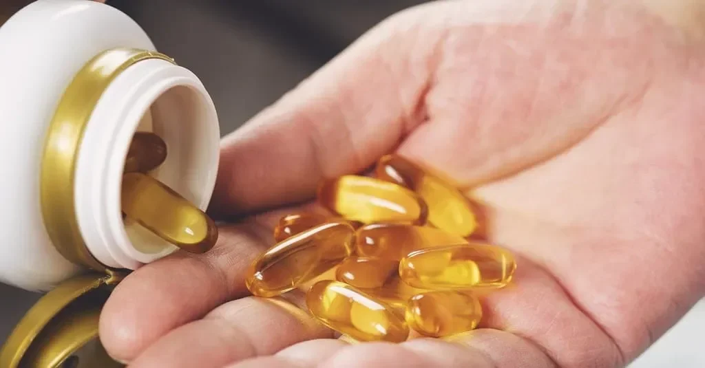 Kapsul suplemen vitamin D tumpah ke tangan dari botol berwarna putih.