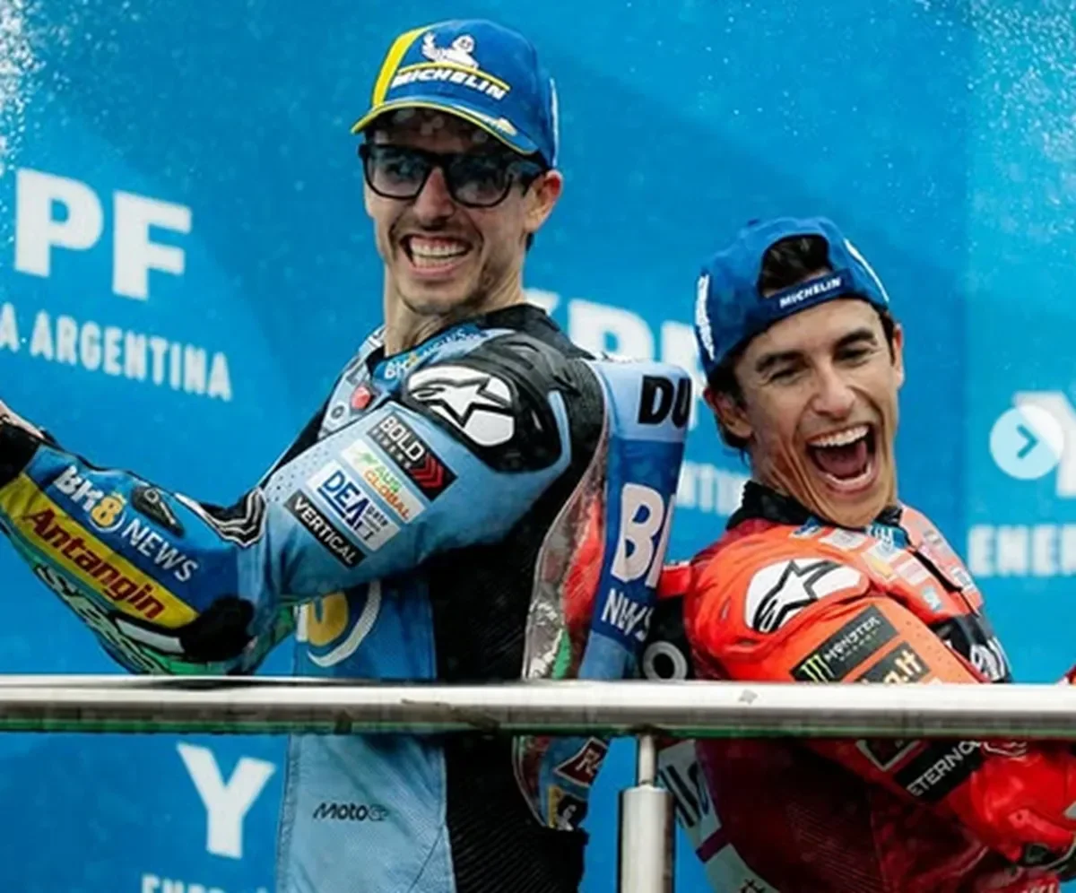 Marc Marquez tersenyum lebar di podium bersama pembalap lain, merayakan kemenangan.