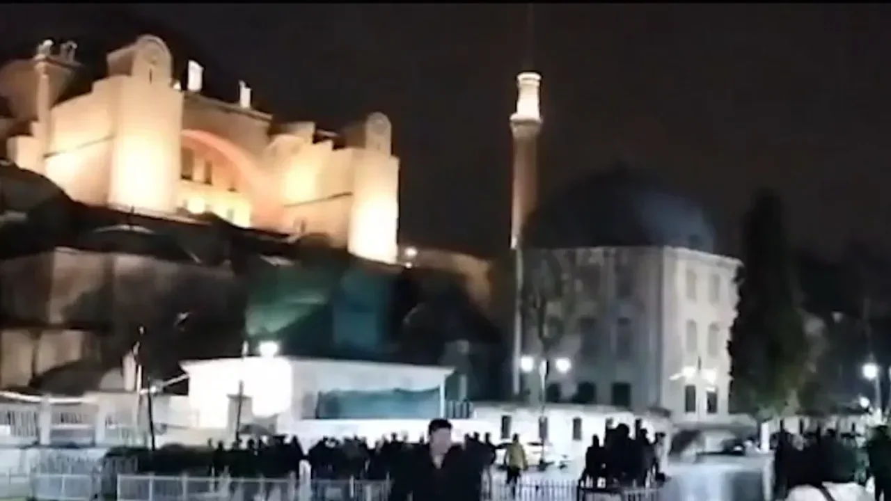 Massa berkumpul di malam hari dengan latar belakang bangunan bersejarah.