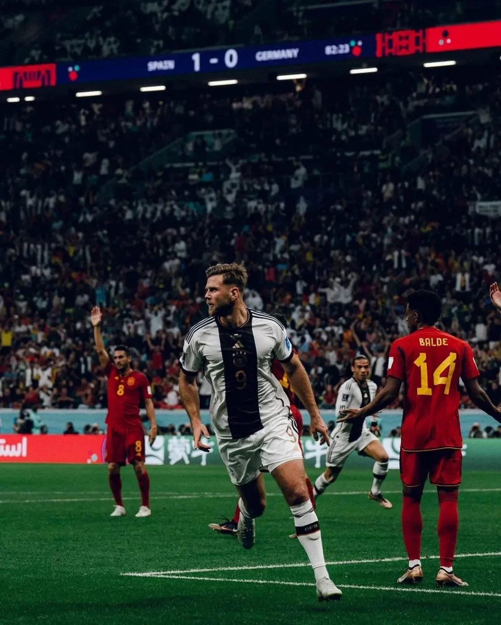 Seorang pemain berjersey putih hitam di lapangan hijau, dengan penonton memadati stadion.