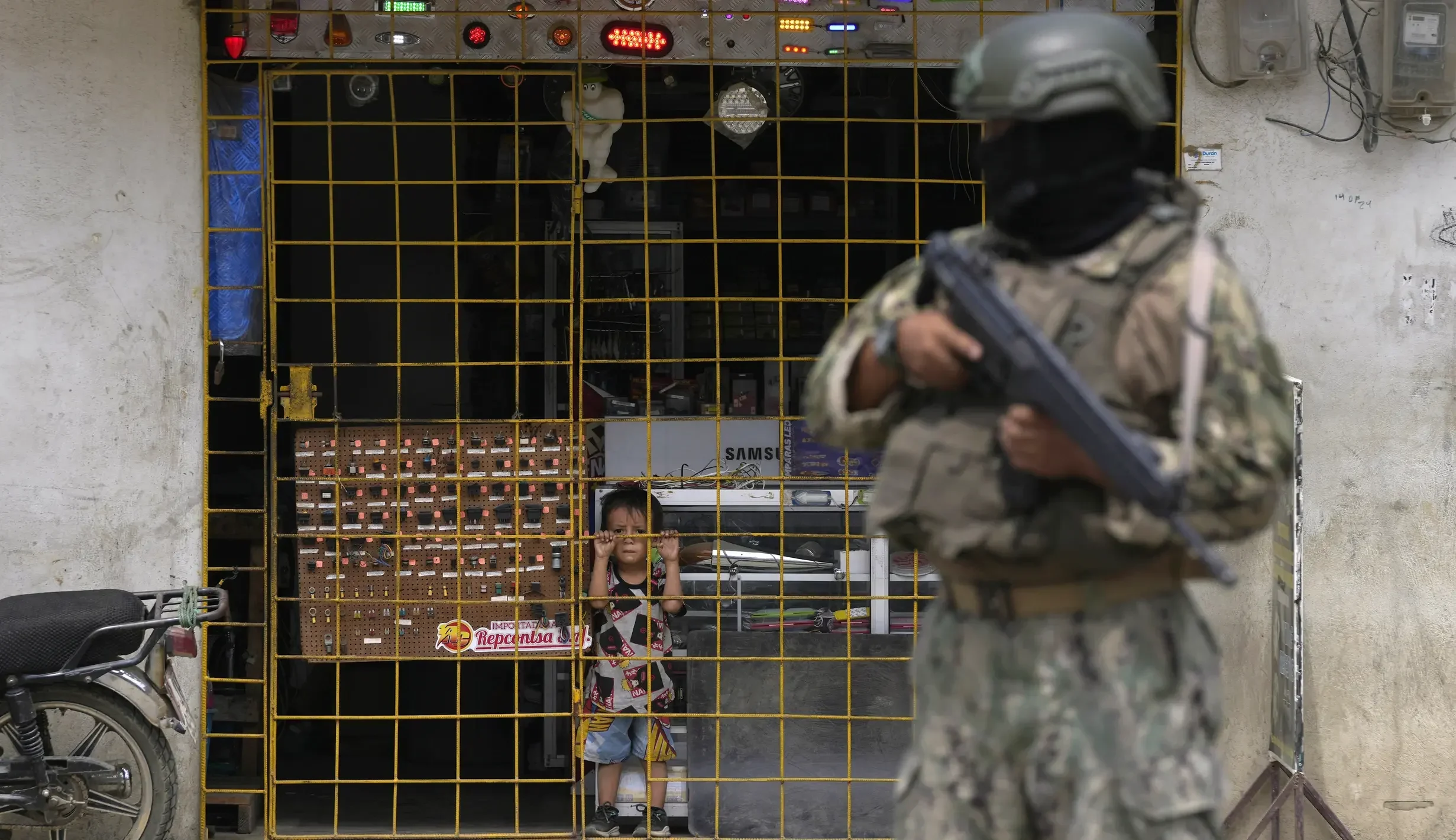 Tentara Ekuador jaga ketat saat anak kecil melihat dari balik jeruji keamanan.