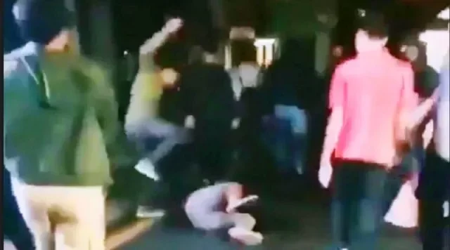 Orang-orang terlibat perkelahian jalanan, satu individu tergeletak di tanah.