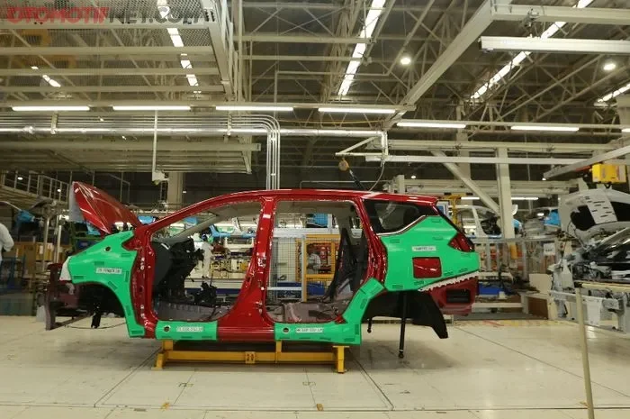 Kerangka mobil Nissan merah sedang dirakit di pabrik otomotif.