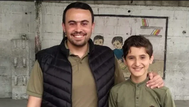 Dua pria tersenyum dengan latar belakang mural anak-anak yang digambar.