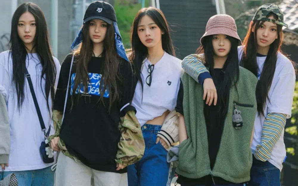 Grup K-Pop NewJeans berpose bersama di luar ruangan, dengan kelima anggota terlihat.