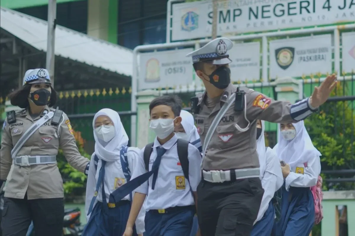 Polisi Indonesia berseragam mengawal siswa sekolah bertopeng di jalanan kota.