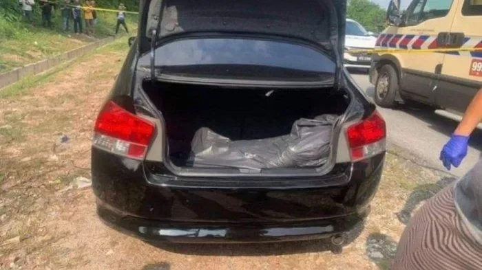 Bagasi mobil hitam terbuka memperlihatkan bungkusan mencurigakan, polisi bersiap.