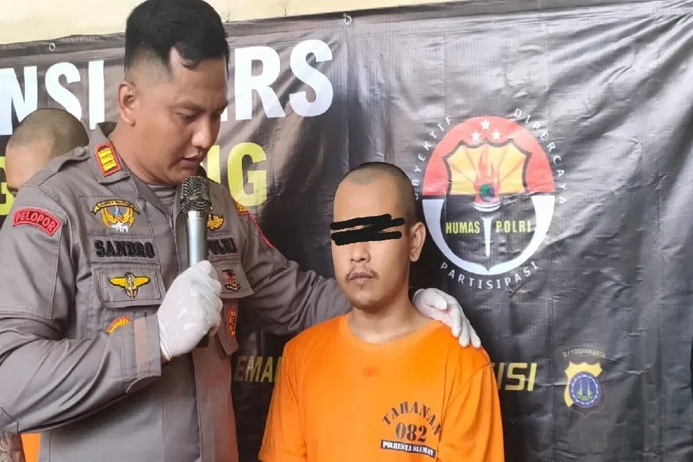 Pria berseragam polisi menginterogasi seorang tahanan dengan latar belakang kain hitam bertuliskan "HUMAS POLRI".