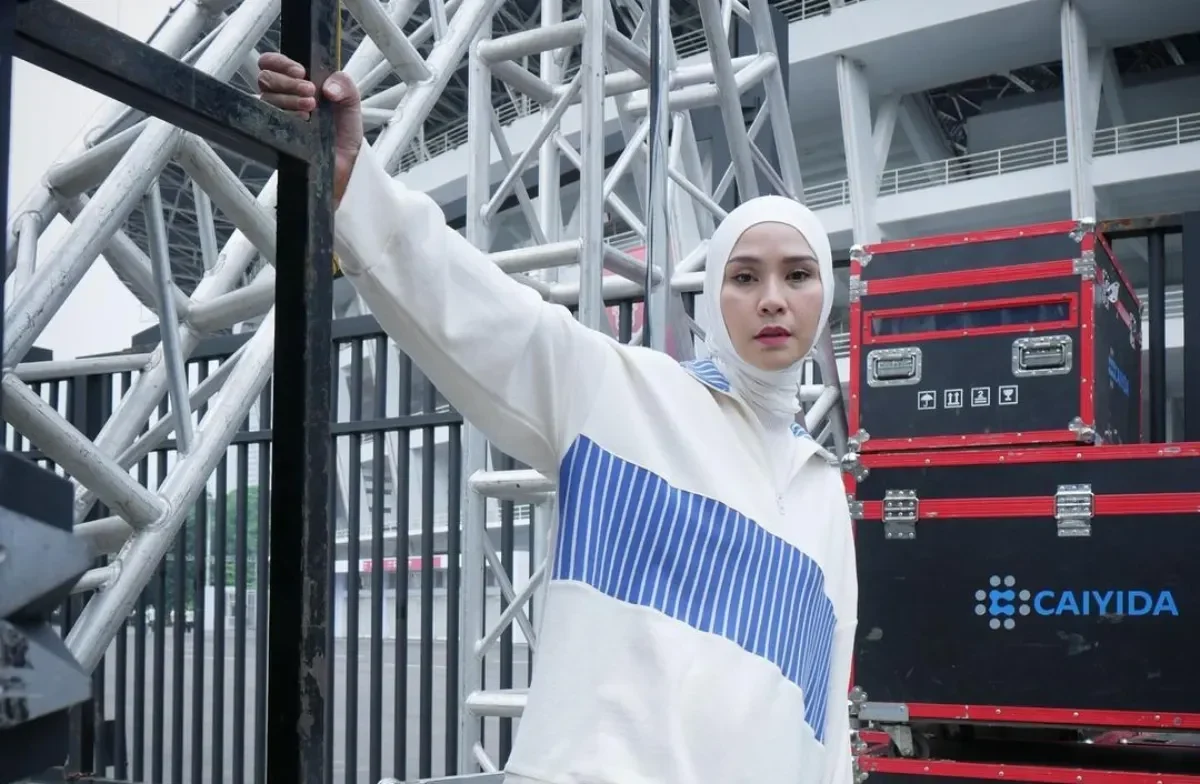 Seorang wanita mengenakan kerudung putih dan pakaian olahraga putih bergaris biru.