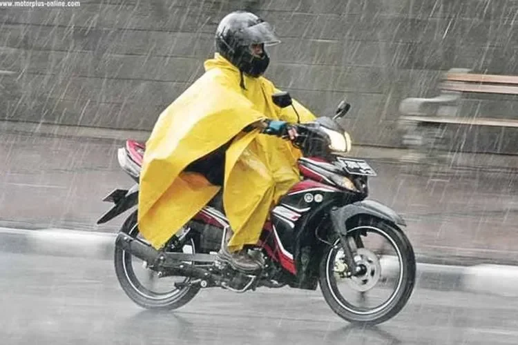 Pengendara motor mengenakan jas hujan ponco kuning saat hujan deras.