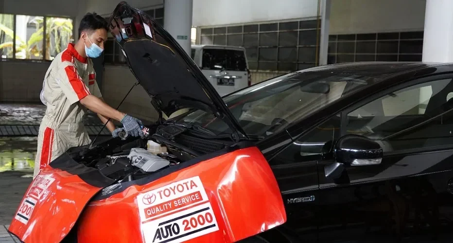 Montir Auto2000 melakukan servis berkala pada mobil Toyota dengan kap terbuka.