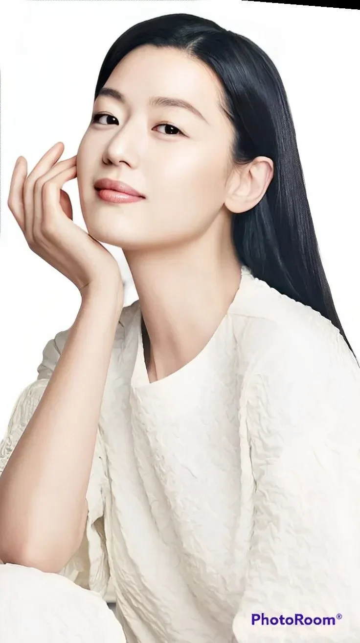 Jun Ji-hyun, aktris Korea Selatan, tersenyum sambil menyentuh wajahnya, mengenakan pakaian putih.