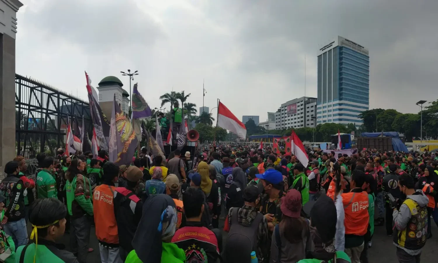 Ribuan pengemudi ojol unjuk rasa di depan Gedung DPR RI membawa bendera dan spanduk.