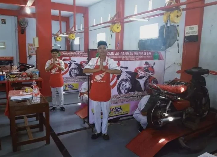 Dua teknisi berapron Honda memberi salam di area bengkel dengan motor dan banner SMK.