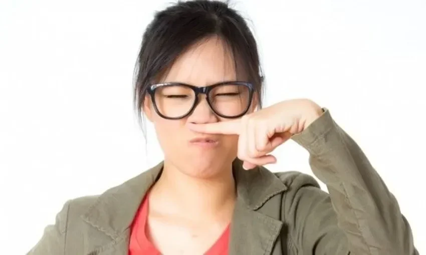 Seorang wanita mencubit hidungnya dengan ekspresi jijik, menggambarkan bau tidak sedap.