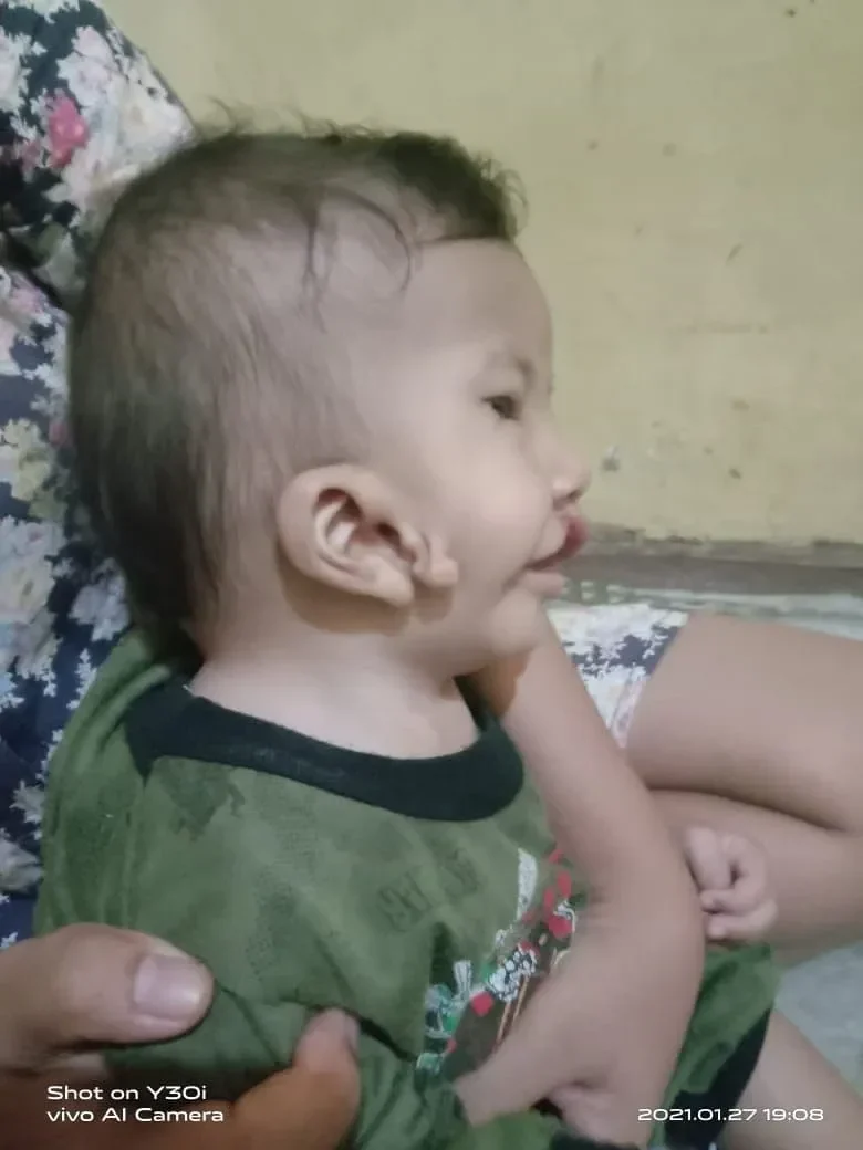 Bayi lucu mengenakan kaus hijau, menampilkan ekspresi ceria dan imut.