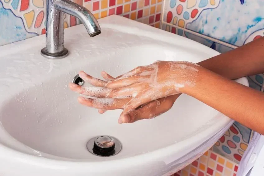 Tangan sedang dicuci dengan sabun di wastafel, busa sabun terlihat jelas.