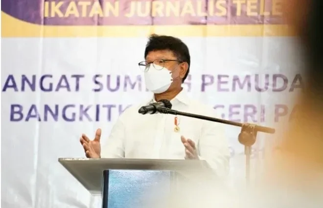 Narasumber berbaju putih berbincang di podium, latar belakang tulisan acara.