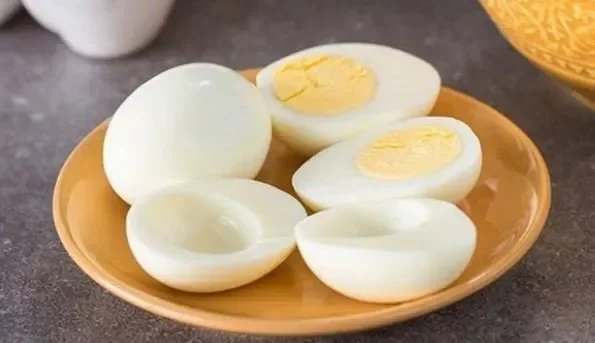 Sepiring telur rebus utuh dan belah dua, disajikan di atas piring oranye.