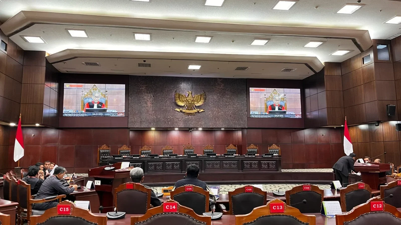 Ruang sidang Mahkamah Konstitusi dengan tayangan hakim dan lambang negara.