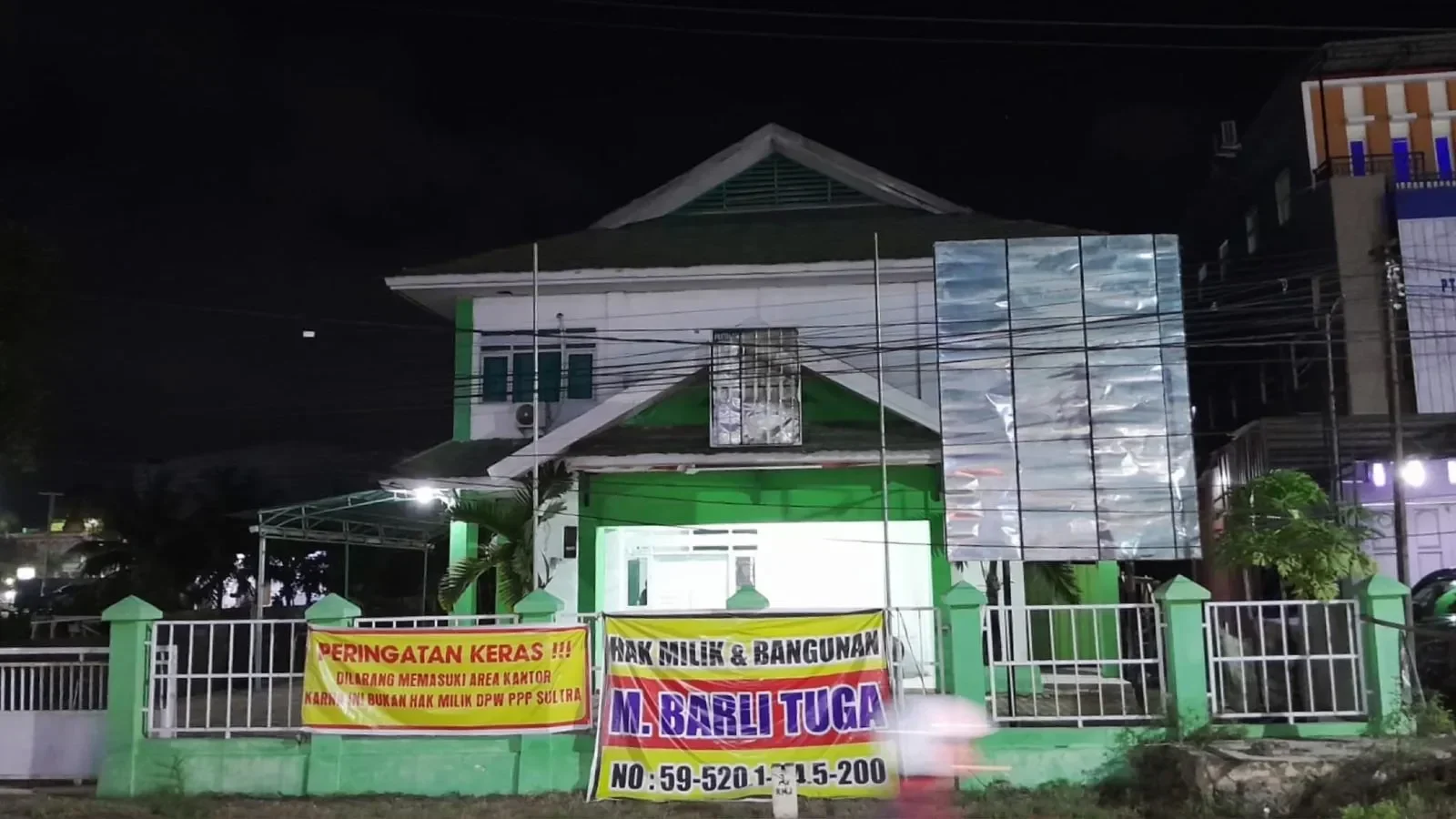 Kantor DPW PPP Sulawesi Tenggara pada malam hari dengan spanduk peringatan.